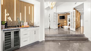 A modern kitchen with white cabinets, a marble countertop, and a wooden accent wall. - Amazing- Ultra Luxe Estate, Resort like Pool, Firepit & More (Palm Springs)