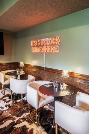 A corner of a room with a neon sign that reads "IT'S 5 O'CLOCK SOMEWHERE" and four white chairs around a small table with a lamp. - Omaha Oasis! Pool, Hot Tub, Mini Golf, Bar, Games (Omaha)
