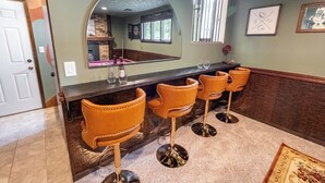 A bar area with a long counter, three orange bar stools, a large mirror, and a window with bars. - Omaha Oasis! Pool, Hot Tub, Mini Golf, Bar, Games (Omaha)