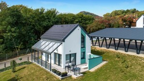 A modern two-story house with a sloped roof, large windows, and a covered outdoor seating area. - 2 bedroom cozy home in Margecan (Margecan)