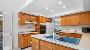 Une cuisine moderne avec des meubles de rangement en bois, une cuisinière encastrée et un grand évier bleu.