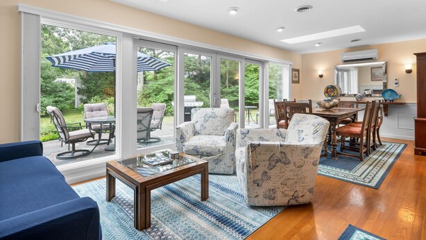 Un vaste espace de vie avec une grande porte vitrée donnant sur un patio, un coin repas avec des meubles en bois et une cuisine avec vue.