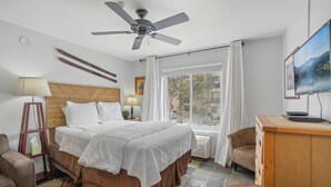 A hotel room with a bed, a desk, a chair, a TV, a ceiling fan, and a window with curtains. - Comfortable Studio in the Heart of Park City (Park City)