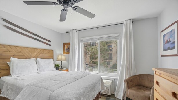 A hotel room with a bed, a chair, a dresser, a ceiling fan, a window with curtains, and a picture on the wall. - Comfortable Studio in the Heart of Park City (Park City)