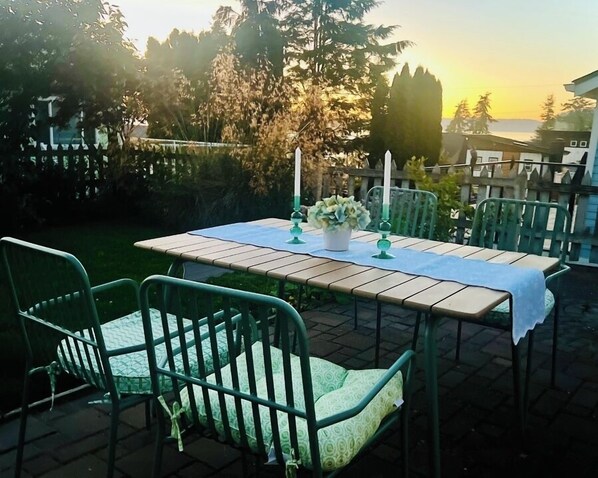 An outdoor patio with a table set for two, surrounded by green metal chairs with cushioned seats. - Camano Island Cottage - Madrona Beach (Camano Island)