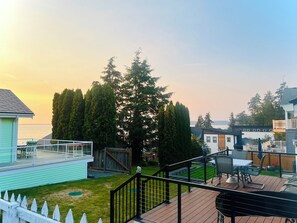 A residential backyard with a patio, a wooden deck, and a view of the ocean. - Camano Island Cottage - Madrona Beach (Camano Island)