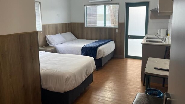Habitació d'hotel amb dos llits, un petit cuina i una finestra amb persianes.