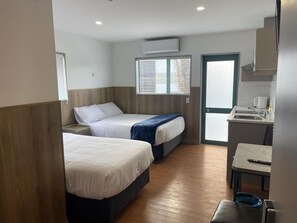 A hotel room with two beds, a kitchenette, and a window with blinds. - Conway Motel (Auckland)