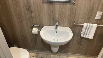 Een badkamer met een houten wand, een witte wastafel, een toilet en een handdoekhouder.
