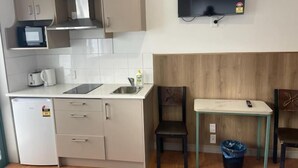 Cuina compacta amb microones, torradora i rentapelats. Hi ha un frigorífic petit, una taula de fusta amb una cadira, i un televisor fixat a la paret.