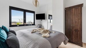 Ein Schlafzimmer mit einem großen Bett, einem an der Wand montierten Fernseher, einem Kleiderschrank und einem Fenster mit Blick ins Freie.