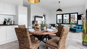 Eine moderne Küche mit weißen Schränken, einem runden Holztisch, Korbstühlen und schwarzen Pendelleuchten.