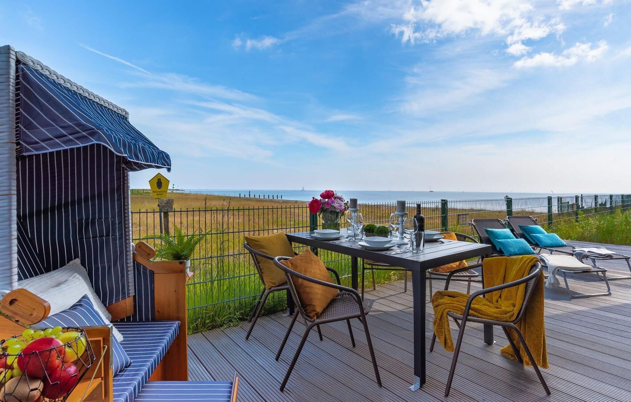 Una terraza con mesa lista para comer, sillas y vista al mar.