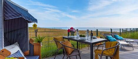 Una terraza con mesa lista para comer, sillas y vista al mar.