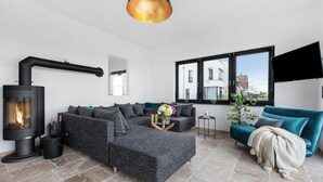 Ein modernes Wohnzimmer mit einem Ecksofa, einem Kamin, einem großen Fenster mit Blick auf die Stadt und einem an der Wand montierten Fernseher.