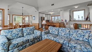 A spacious living area with a large floral-patterned sofa, wooden coffee table, and dining area with chairs and a table. - 7865- Peridot, Oceanfront 5 bedroom home in Frisco! (Frisco)