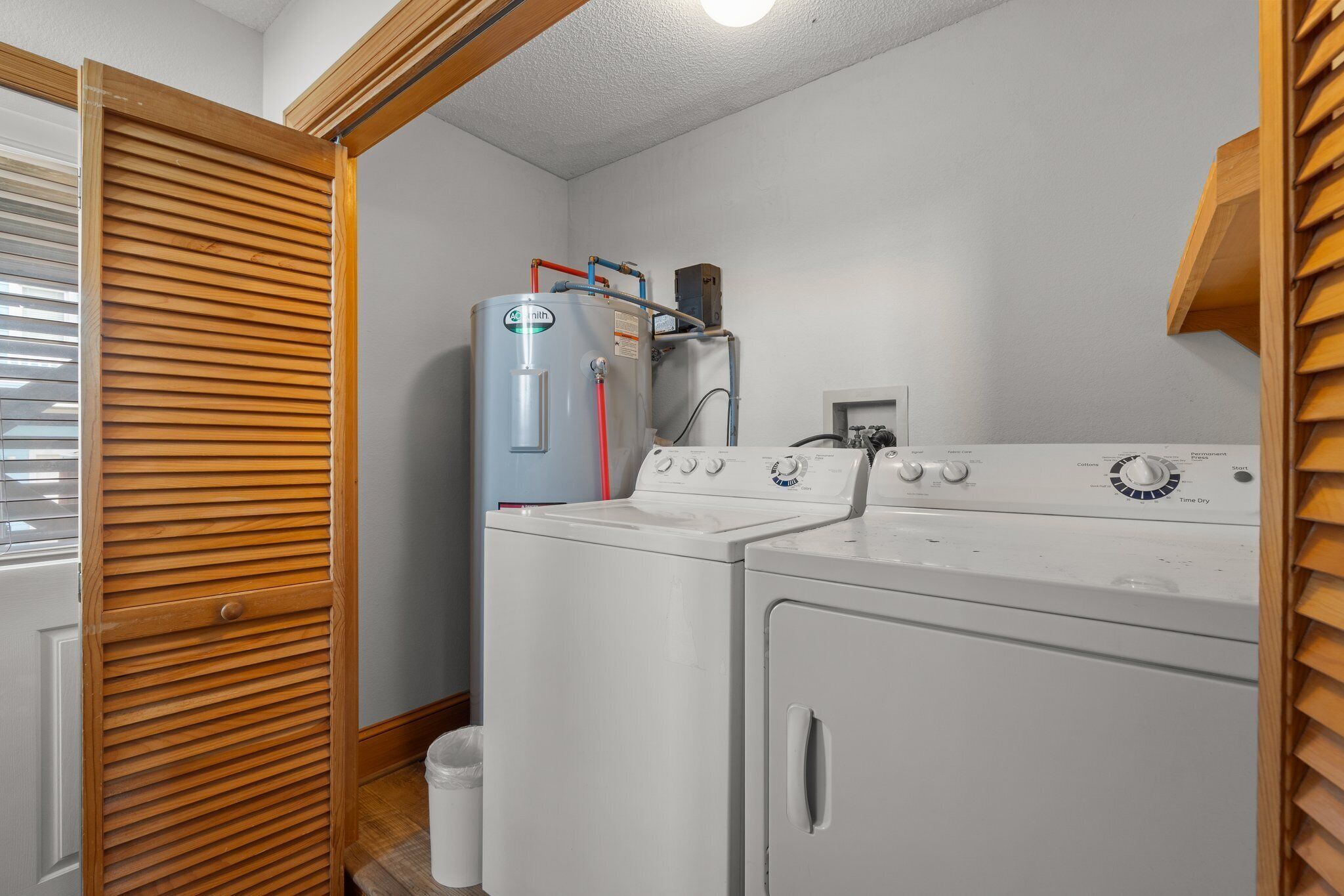 Une buanderie équipée d’un lave-linge et d’un sèche-linge à chargement frontal, d’un chauffe-eau et d’une porte en bois à lattes horizontales.
