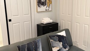 Ein modernes Zimmer mit grauem Sofa, abstrakten Bildern an der Wand und einem schwarzen Beistelltisch mit Handtüchern.