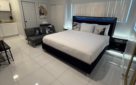 A modern bedroom with a large bed, a sofa, a desk, and a window with blinds.