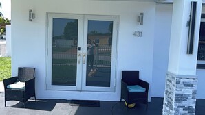 Ein überdachter Balkon mit einer Schiebetür, zwei Korbstühle und einer Steinsäule.