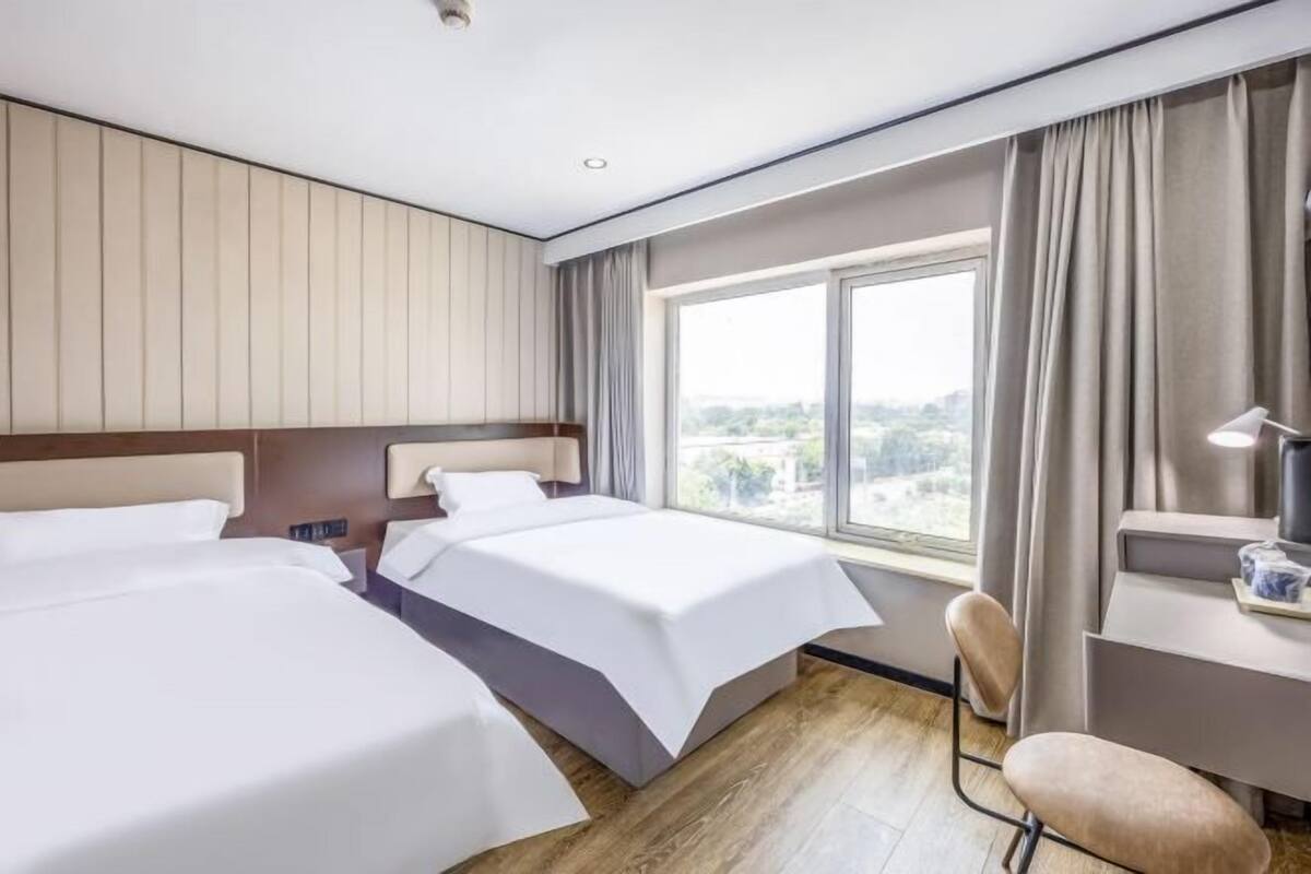 Et hotelværelse med to senge, et skrivebord, en stol og et stort vindue.