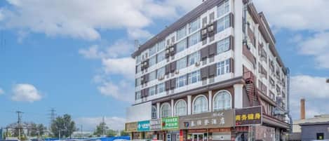 A multi-story building with commercial establishments on the ground floor, a parking lot in front, and a clear sky.