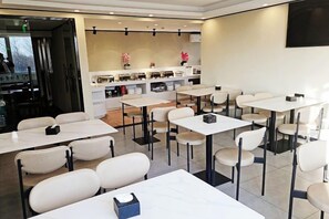 A modern dining area with multiple tables and chairs, a kitchen counter, and a flat-screen TV mounted on the wall. - Taishangdeng Hotel (Beijing Daxing Huangyi Road Public Security University Branch) (Beijing)
