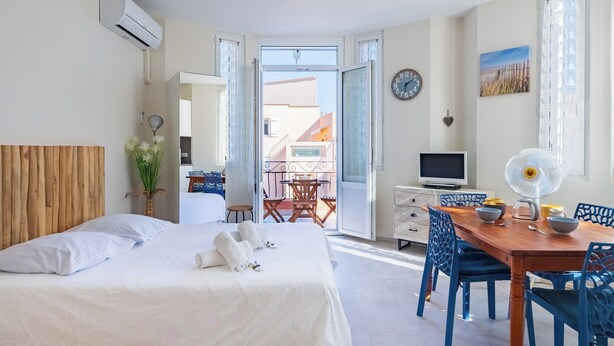 A hotel room with a bed, a dining table with chairs, a TV, and an air conditioning unit. - Studio de la Villa 2 étoiles - Welkeys (Bandol)