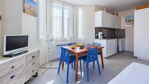 A modern room with a dining table, blue chairs, a TV, and a kitchen area. - Studio de la Villa 2 étoiles - Welkeys (Bandol)
