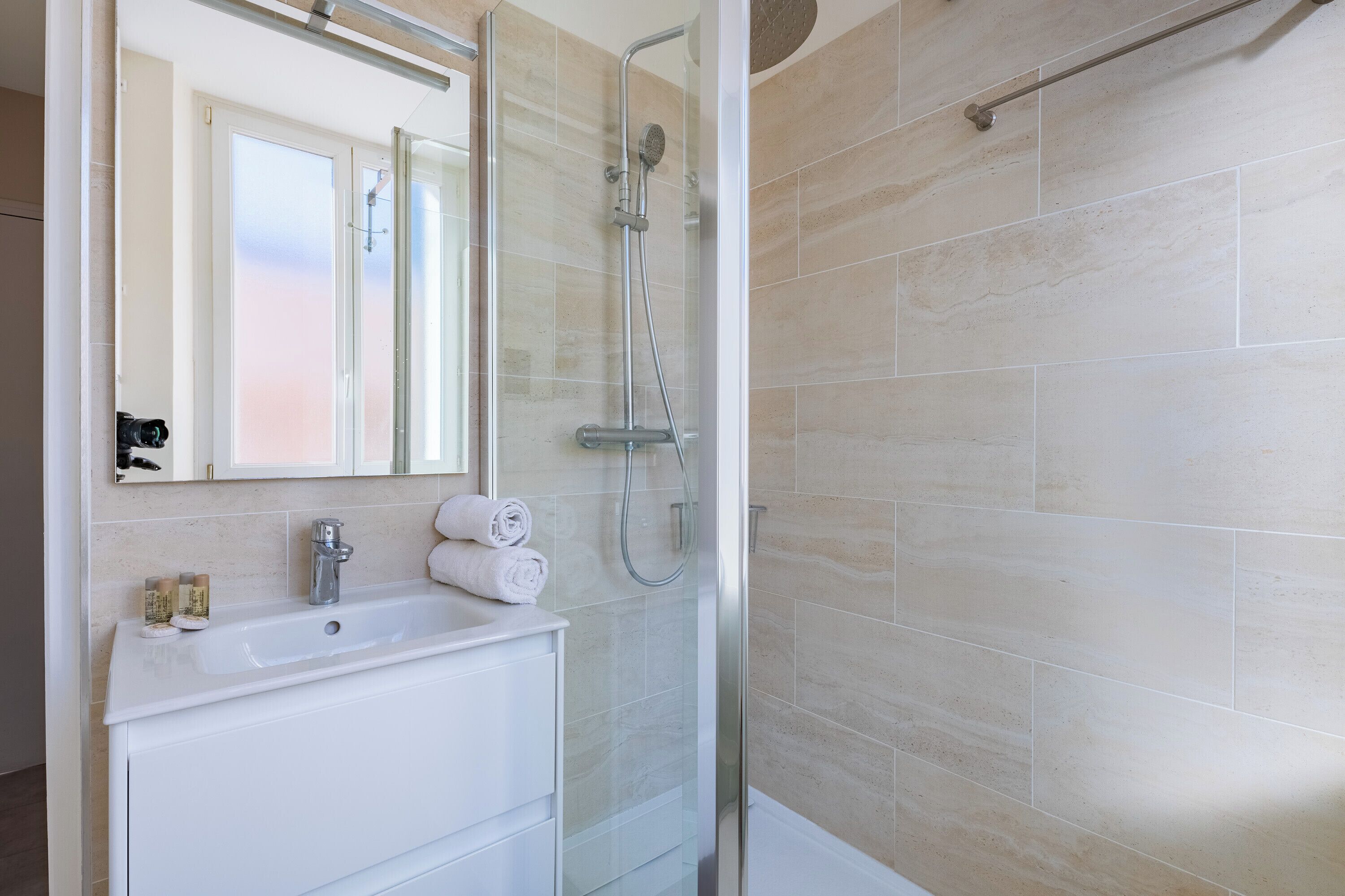Un baño moderno con ducha de vidrio, un lavamanos blanco y un espejo encima.