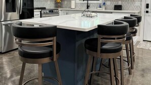 Una cucina moderna con mobili bianchi, un frigorifero in acciaio inossidabile, forno integrato e una grande isola con sgabelli da bar.