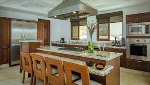 A modern kitchen with a central island, wooden chairs, stainless steel appliances, and a large window.