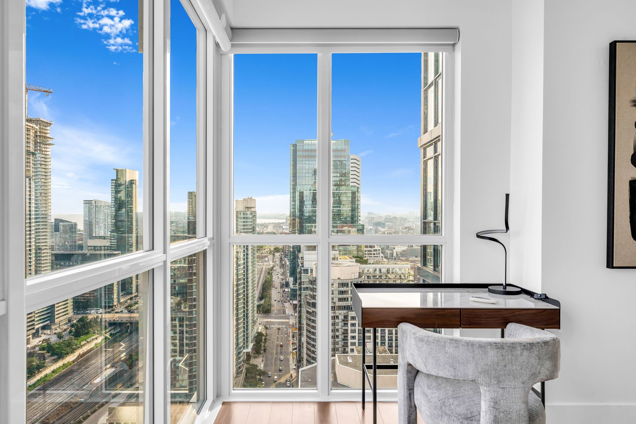 A room with a large window offering a city view, a desk, and a chair.