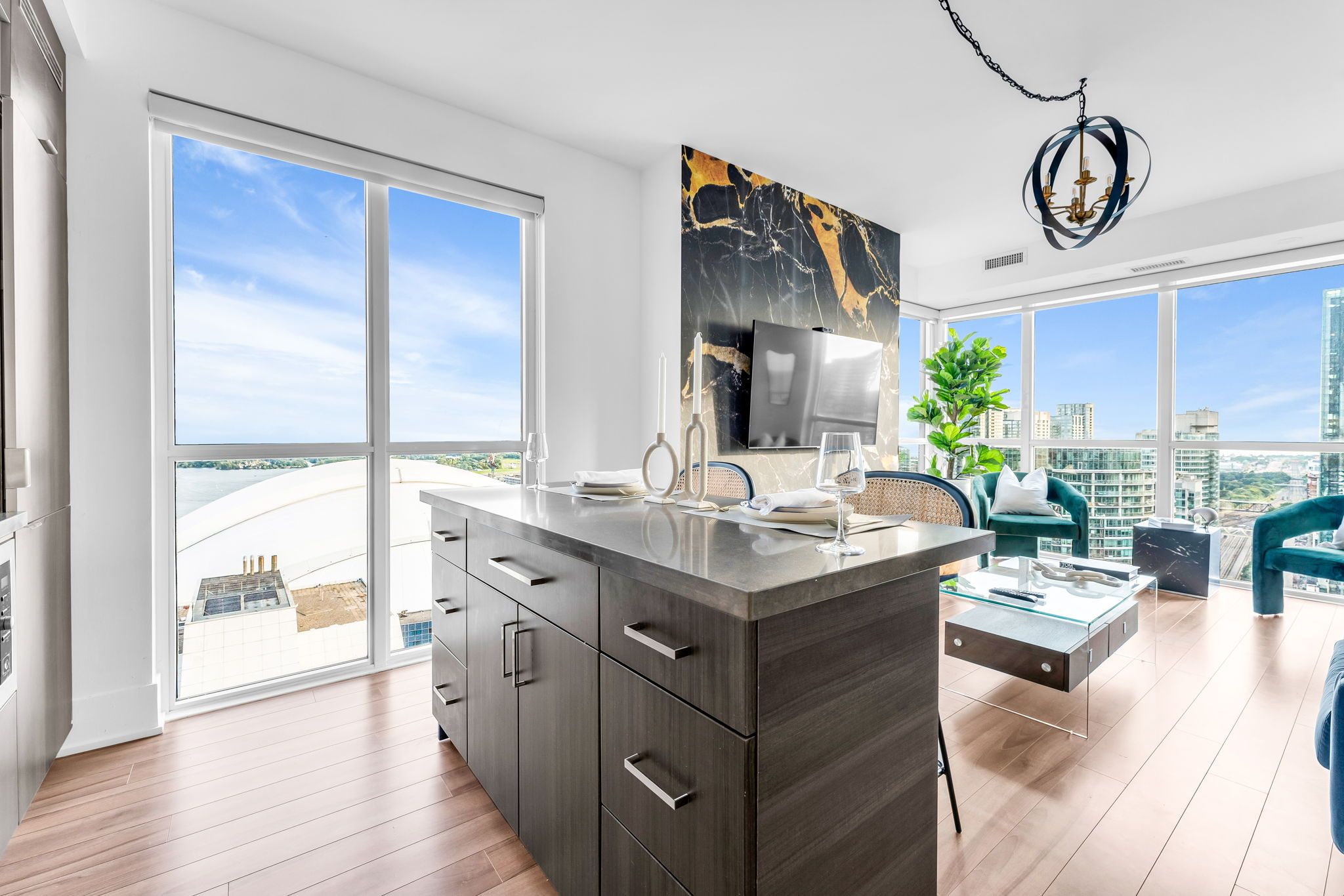 A modern kitchen with a large island, a dining area with a view, and a living space with a sofa and a plant.