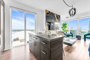 Eine moderne Küche mit einer großen Kochinsel, einem Essbereich mit Aussicht und einem Wohnbereich mit Sofa und Pflanze.