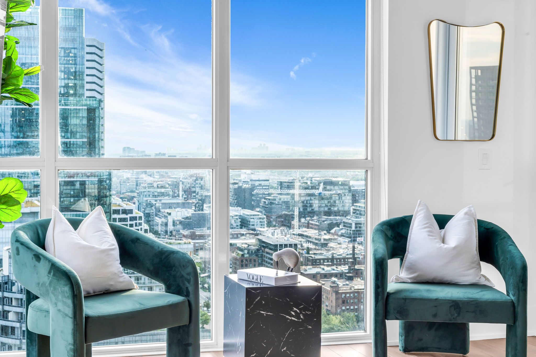 A modern room with two green armchairs, a marble side table, and a large window offering a city view.