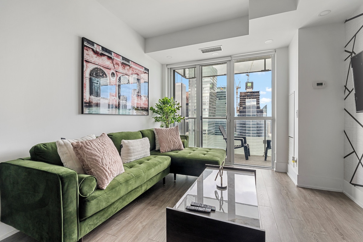 Ein modernes Wohnzimmer mit einem grünen Sofa, einem Glastisch und einem großen Fenster mit Blick auf die Stadt.