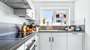 Une cuisine moderne avec un plan de travail noir, des meubles blancs et une fenêtre donnant sur un immeuble.