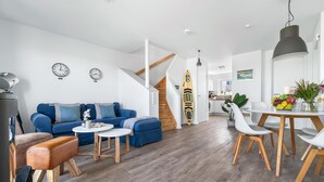 Un salon moderne avec un canapé bleu, une table basse en bois et un coin repas comprenant des chaises blanches et une table en bois.