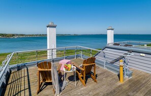 A deck with two wooden chairs and a small table, overlooking a body of water with a distant shoreline.