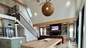 Een ruime woonkamer met een grote houten tafel, een trap en een moderne keuken.