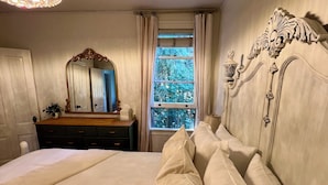 A bedroom with a large bed, a dresser, a mirror, and a window with a view of trees.