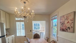 A spacious kitchen with a wooden dining table, white cabinets, a chandelier, and a large floral painting on the wall.