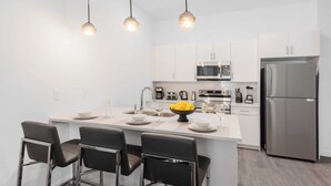 Une cuisine moderne avec des armoires blanches, des appareils en acier inoxydable et des tabourets de bar noirs.