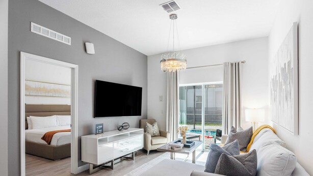 Une chambre d’hôtel moderne équipée d’un lit, d’un téléviseur à écran plat, d’une console blanche, d’un canapé, d’une table basse et d’un lustre.