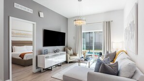 A modern hotel room with a bed, a TV, a sofa, a coffee table, and a view of a swimming pool. - Parkside Serenity by Avantstay Private Pool! (Davenport)