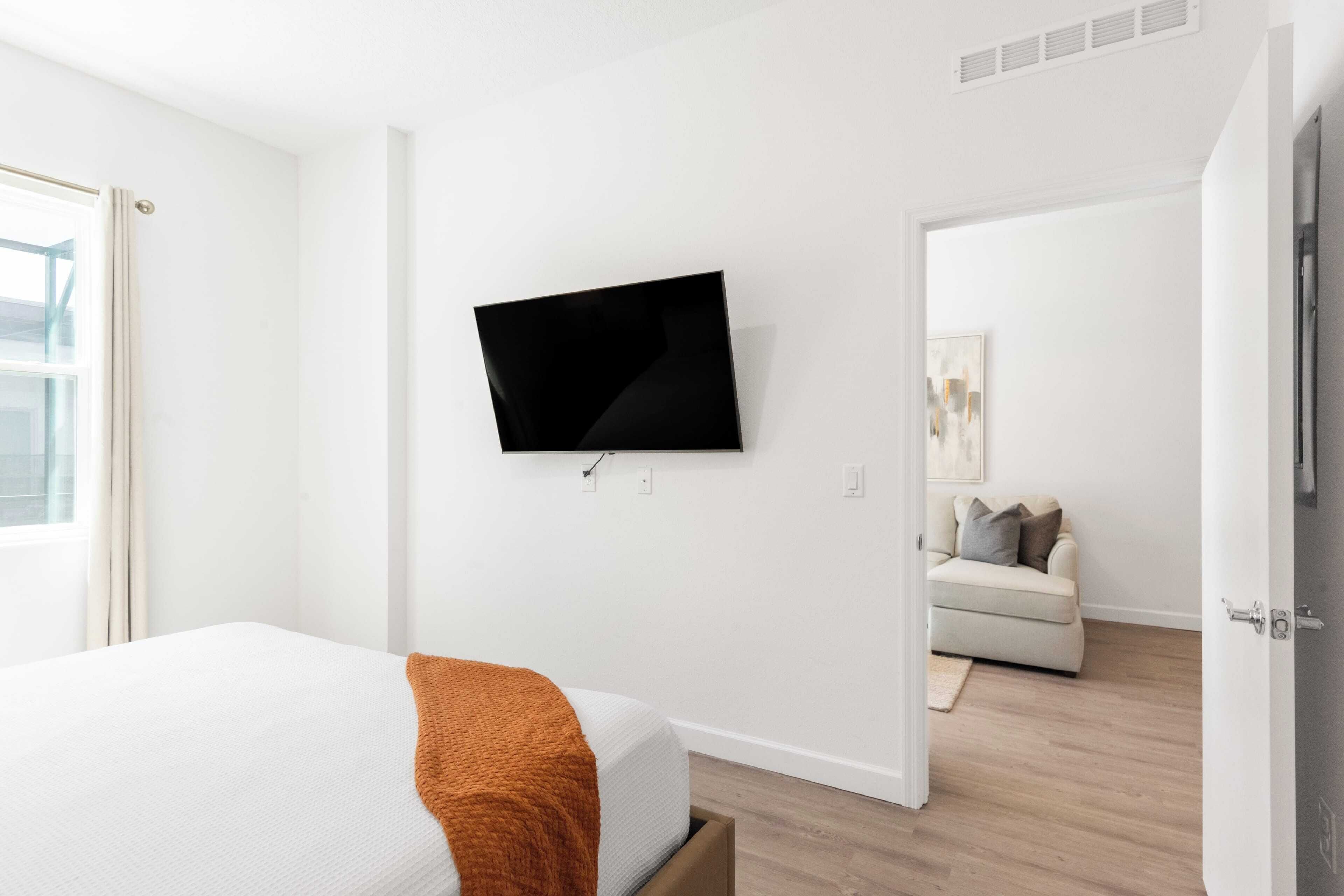 Ein modernes Hotelzimmer mit einem Bett, einem an der Wand befestigten Flachbildfernseher, einer Couch im Hintergrund und Holzboden.