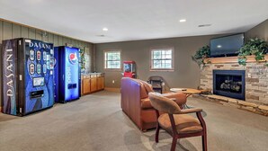 A living room with a fireplace, a leather sofa, a television, and vending machines. - New Home in Trophy Run with Private Hot Tub & Firepit, Near Taneycomo & Table Rock, Free Tickets (Branson)