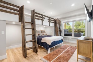 Una camera da letto con un letto a castello, una scala in legno, un comodino, una televisione e una finestra vista alberi.
