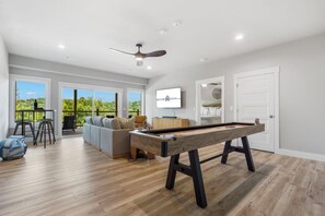 A modern living room with a pool table, a sofa, and a TV mounted on the wall. - New Home in Trophy Run with Private Hot Tub & Firepit, Near Taneycomo & Table Rock, Free Tickets (Branson)